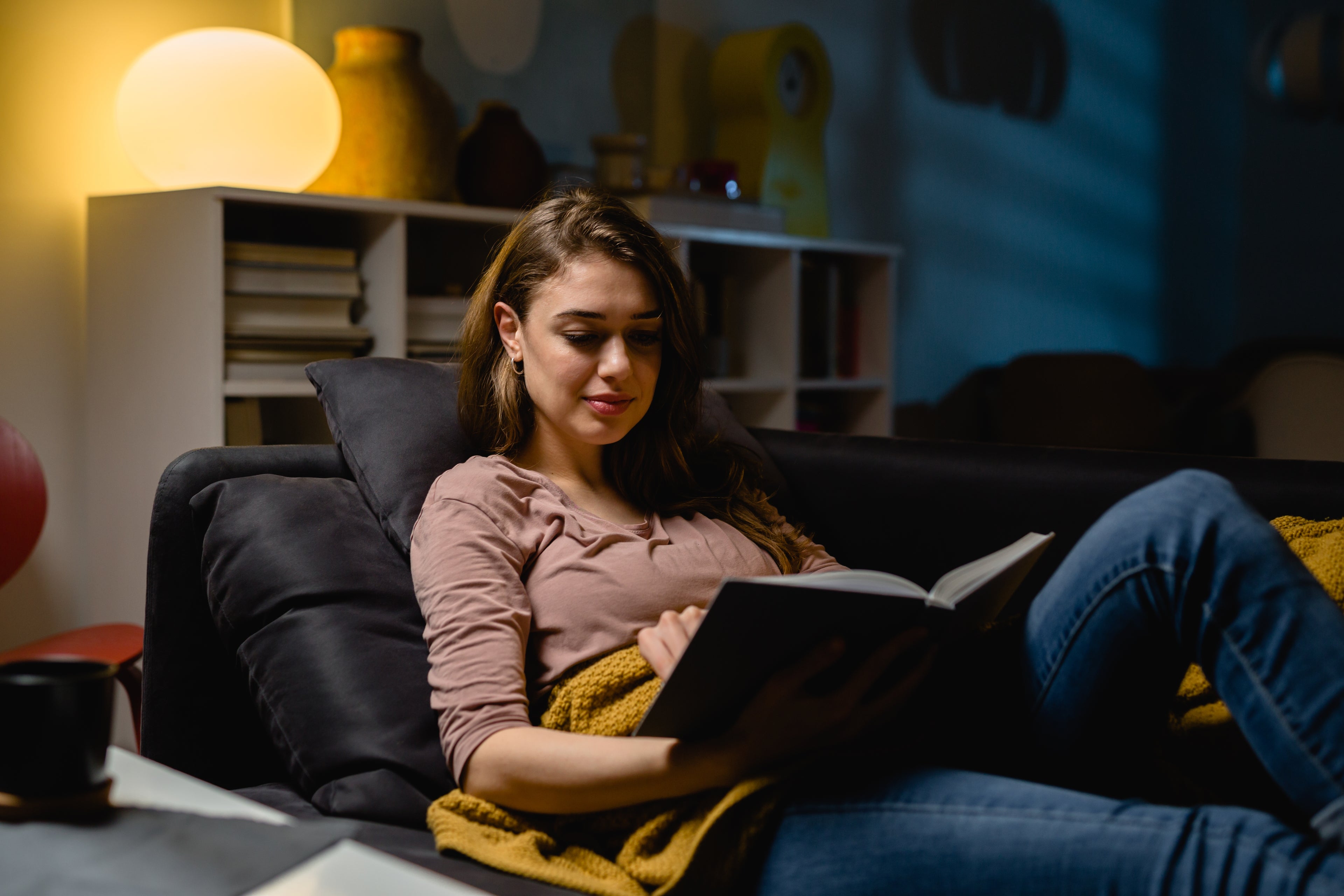 Women reading Blindly blind date with a book in a low lit room on a couch.